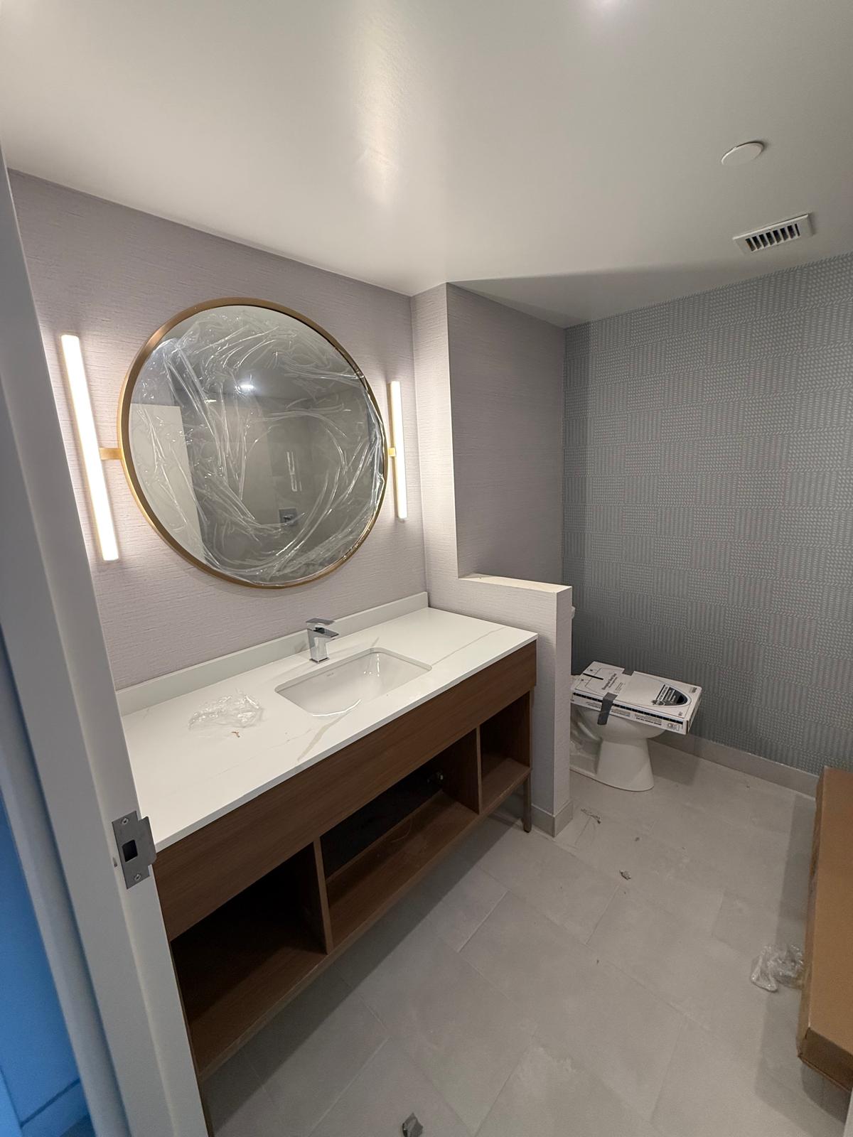 Finished commercial washroom with custom wood vanity, round mirror and textured wall finishes