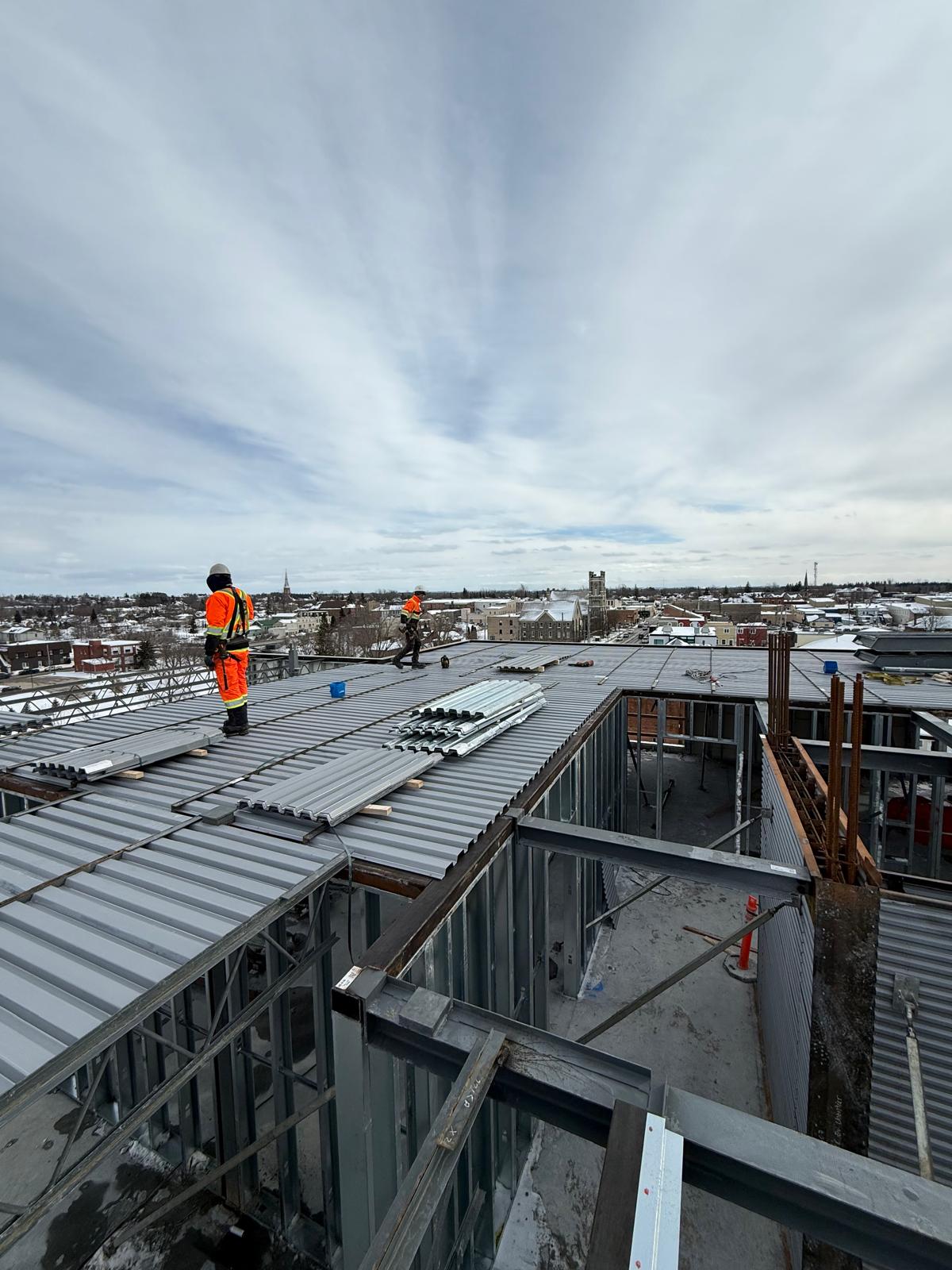 Crew installing steel roof decking over light-gauge framing in winter