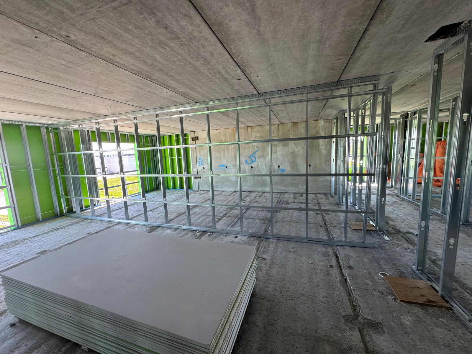 Interior commercial partition walls framed with light-gauge steel studs beside stacked drywall