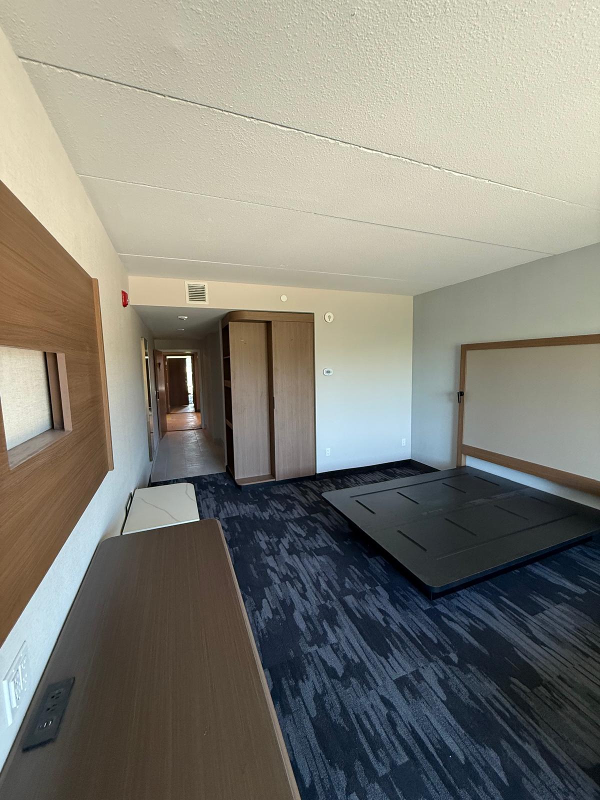 Finished hospitality guest room with acoustic ceiling, wall panels, carpet and built-in furniture