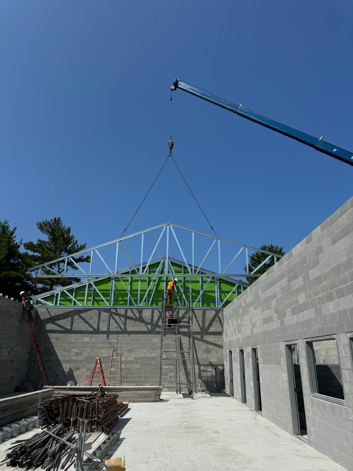 Workers landing steel roof trusses inside a block building