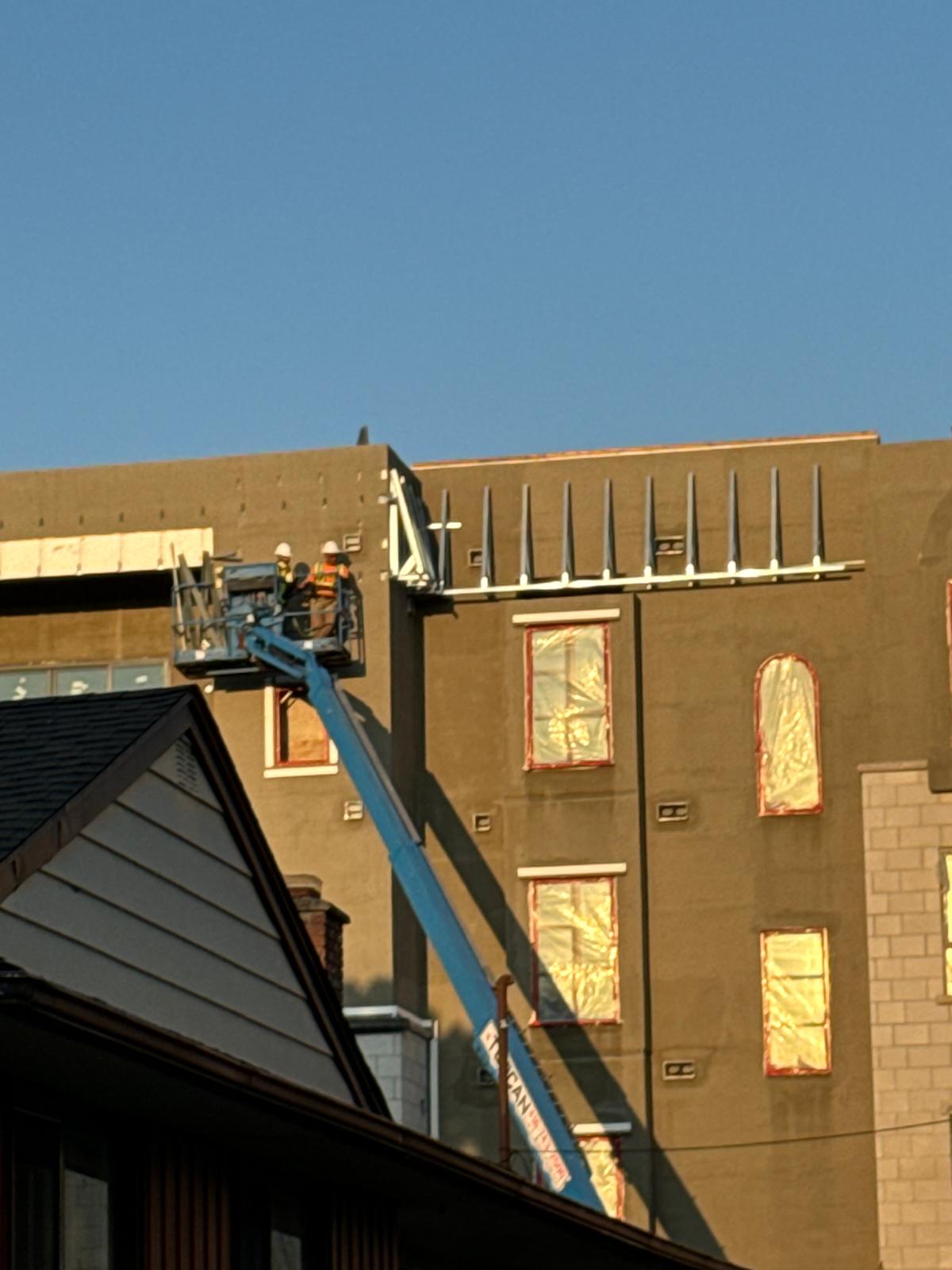 Crew on a boom lift installing roof edge framing at sunset